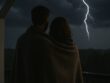a man and woman wrapped in a blanket looking at lightning